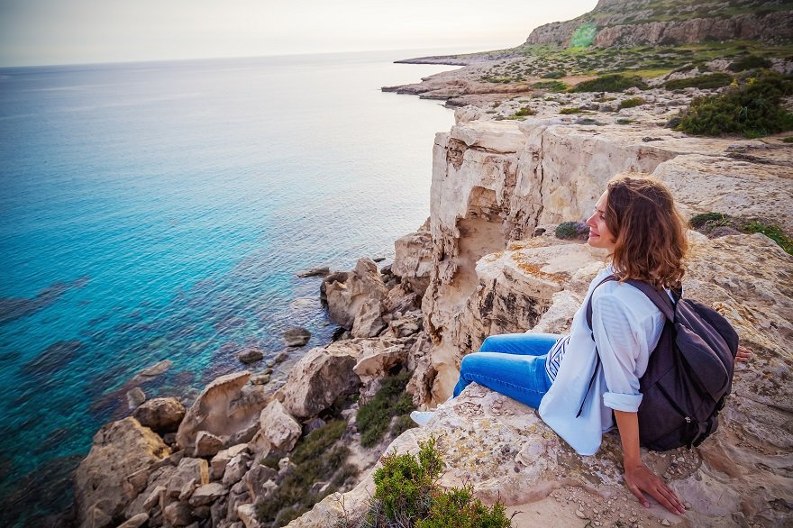 Moving to Cyprus - A young female traveler watches a beautiful sunset on the rocks and beach, Cape Greco, Cyprus